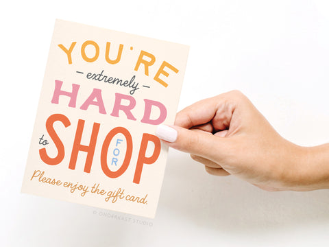 A hand with light-pink nails holds Onderkast Studio’s Youre Hard to Shop For Greeting Card, featuring colorful, playful text on a premium cream background for a fun touch.