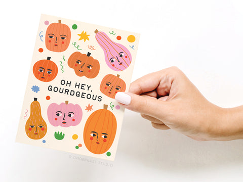 A hand holds the Oh Hey Gourdgeous Greeting Card by Onderkast Studio, featuring pumpkins and gourds with faces, colorful confetti, and bold OH HEY GOURDGEOUS text.