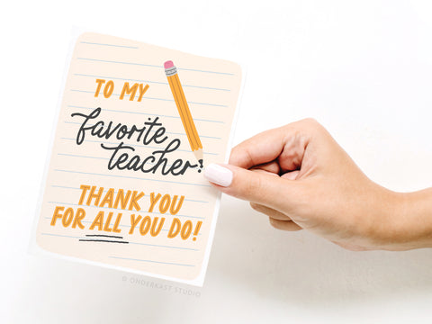 A hand holds the Onderkast Studio To My Favorite Teacher Greeting Card, featuring a pencil drawing, lined paper background, and the message “To my favorite teacher! Thank you for all you do!” Printed in the USA.