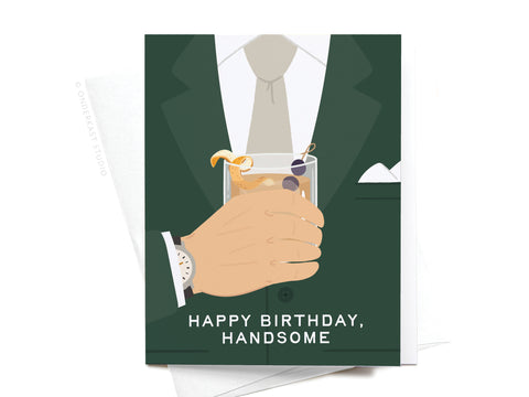 The Happy Birthday Handsome Greeting Card by Onderkast Studio features a light-colored illustration of a man’s green-suited hand holding a cocktail, with HAPPY BIRTHDAY, HANDSOME at the bottom—a perfect premium birthday greeting.