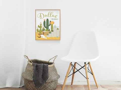 The Dallas Succulent Skyline Art Print by Onderkast Studio adds desert chic vibes to a minimalist room, displayed on a white wall beside a modern chair and woven basket with blanket, blending cacti and cityscape in stylish décor.