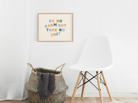 A white modern chair sits beside a woven basket in a minimalist room. Above, the Onderkast Studio Do No Harm Art Print adds vibrant color and flair with its bold message: DO NO HARM BUT TAKE NO SHIT.