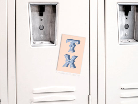 A beige postcard featuring large blue TX letters, inspired by Onderkast Studios TX Refrigerator Magnet, is centered on a white metal locker door between two handles.