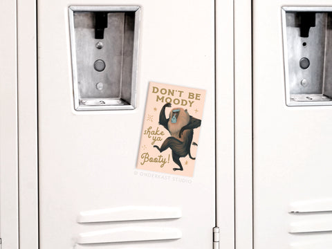 A beige locker displays a playful DONT BE MOODY, shake ya Booty! Dancing Baboon poster, plus extra charm from Onderkast Studios Shake Ya Booty Baboon Refrigerator Magnet on the front.