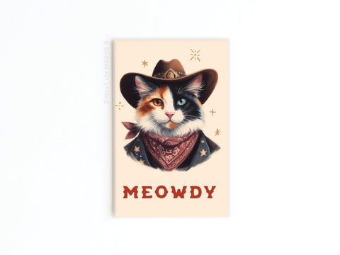 The Meowdy Cowboy Cat Refrigerator Magnet by Onderkast Studio features a cowboy cat in a brown hat and red bandana, MEOWDY in bold red letters, and star doodles on a light beige background—perfect for any feline-themed magnet collection.