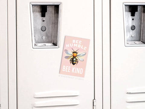 The Bee Humble Bee Kind Refrigerator Magnet by Onderkast Studio features a bee-themed design and the words Bee Humble, Bee Kind, adding a cheerful touch reminiscent of a light-colored locker sticker.