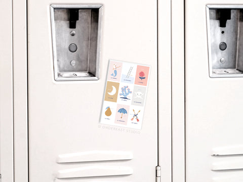 The Onderkast Studio Lotería Refrigerator Magnet decorates a light gray locker door with nine colorful illustrations and labels, inspired by the classic Mexican game, featuring images like a moon, pear, umbrella, and flower.