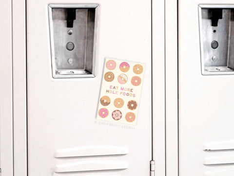 The Hole Foods Donuts Refrigerator Magnet by Onderkast Studio adds a playful touch to your fridge with its colorful design and fun EAT MORE HOLE FOODS text—perfect kitchen decor for donut lovers!.