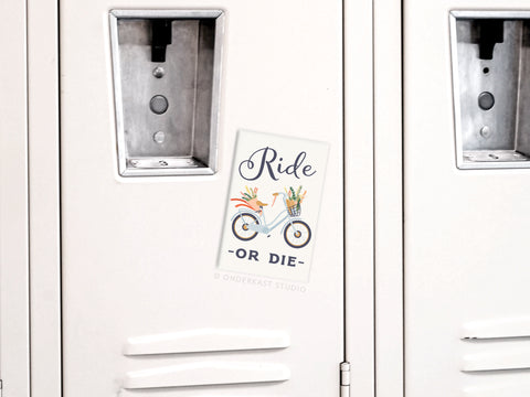 Onderkast Studios “Ride Or Die Bicycle” refrigerator magnet features an illustrated bike with baskets of flowers and vegetables, plus a card that says “Ride or Die,” all on a white locker.