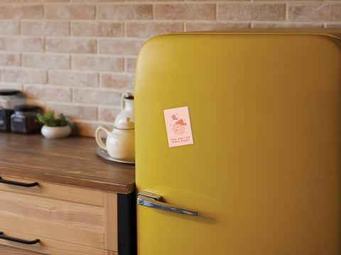 A retro yellow fridge with a stylish design features the vibrant Ain’t My First Disco Refrigerator Magnet by Onderkast Studio in a cozy kitchen with wooden cabinets, jars, a teapot, and a brick wall.