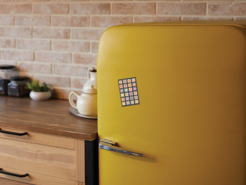 A retro yellow fridge displays the Granny Squares Crochet Blanket Refrigerator Magnet by Onderkast Studio, adding handmade charm to a kitchen with wooden cabinets, a teapot set, jars, and a brick-patterned backsplash.