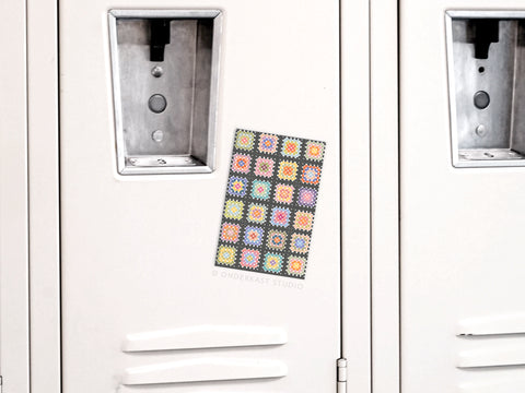 The Onderkast Studio Granny Squares Crochet Blanket Refrigerator Magnet adds a touch of handmade warmth to a white locker door, positioned between two handles.