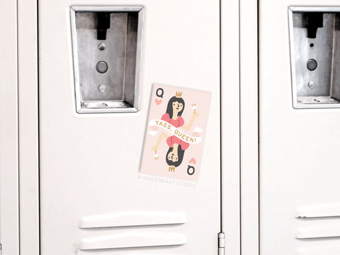 A beige locker displays the Yass Queen of Hearts Refrigerator Magnet by Onderkast Studio, featuring a cartoon queen with a crown, brown hair, raised fists, hearts, and the bold phrase YASS QUEEN! in a regal design.