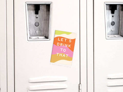 Onderkast Studio’s “Let’s Drink to That” Refrigerator Magnet features bold text on a modern, abstract pastel background with vibrant colors, designed to add a cheerful touch to your white locker or fridge.
