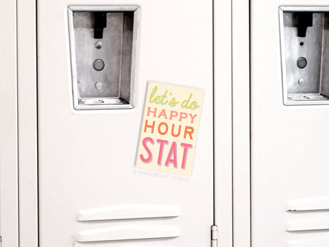 The Onderkast Studio Happy Hour Stat Refrigerator Magnet, featuring lets do HAPPY HOUR STAT, is pinned to a white locker door, adding a playful accent among the lockers.