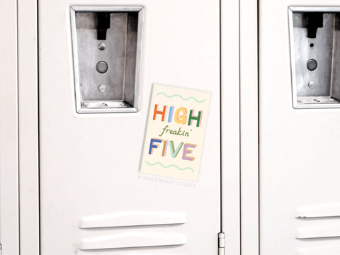 A High Freakin’ Five Refrigerator Magnet by Onderkast Studio with a colorful, vibrant design is displayed on a white locker. The minimal background keeps the focus on its cheerful message and high-quality production.