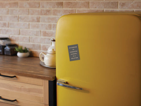 A cozy kitchen with a wooden counter and brick backsplash features a yellow retro-style fridge adorned with Onderkast Studio’s Alcohol Is a Solution Refrigerator Magnet.