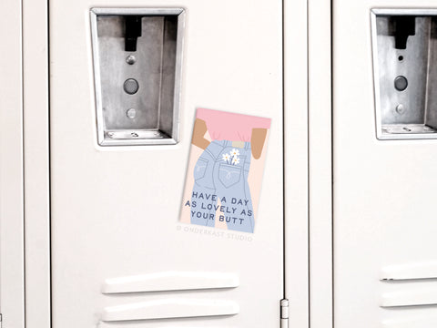 The Onderkast Studio Lovely As Your Butt Refrigerator Magnet features vibrant colors and an illustration of a person in jeans and pink shirt with flowers, plus the phrase: Have a day as lovely as your butt.