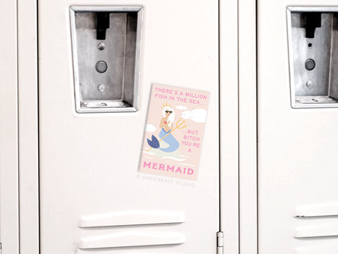 The “Bitch You’re a Mermaid Refrigerator Magnet” by Onderkast Studio features a pink cartoon mermaid postcard and sassy text, making it a fun, quirky addition to your fridge.