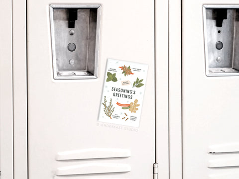 The Seasoning’s Greetings Refrigerator Magnet by Onderkast Studio, featuring festive illustrations of herbs and spices, adds a cheerful holiday touch to a white locker.