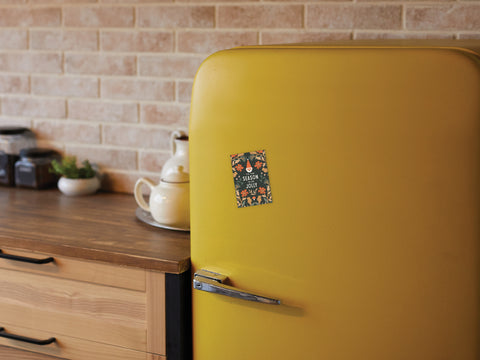A retro yellow fridge displays the Onderkast Studio ’Tis the Season To Be Jolly magnet in a cozy kitchen with a wooden countertop, teapot set, and brick backsplash—adding festive holiday charm in style.