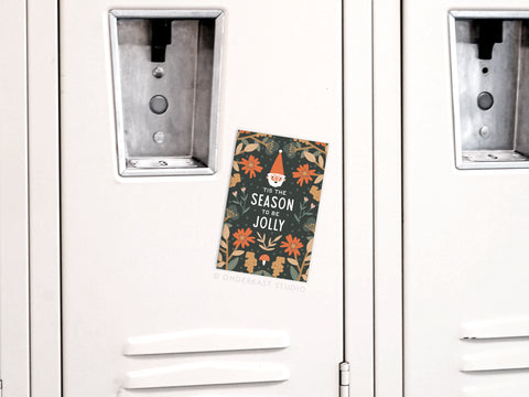 The ’Tis the Season To Be Jolly Refrigerator Magnet by Onderkast Studio, featuring a gnome and florals, is displayed on a white locker door, adding festive cheer and Christmas spirit to the space.