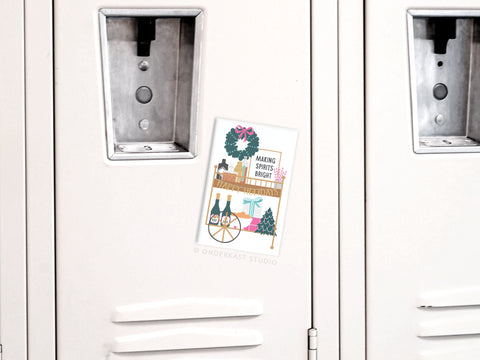 The Onderkast Studio Making Spirits Bright Bar Cart refrigerator magnet features festive decor and attaches cheerfully to a white metal locker.