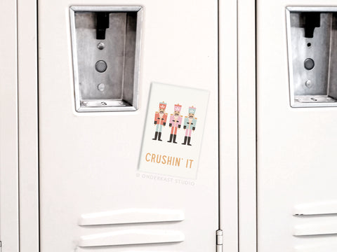 The Crushin’ It Nutcrackers Refrigerator Magnet by Onderkast Studio features three illustrated nutcrackers and playful text, adding festive holiday cheer to your fridge or locker.