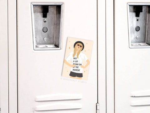 A beige locker holds an Onderkast Studio TS Red Refrigerator Magnet, featuring a woman in sunglasses and a Not a lot going on at the moment shirt—showcasing Taylors charm and quality between the locker doors.