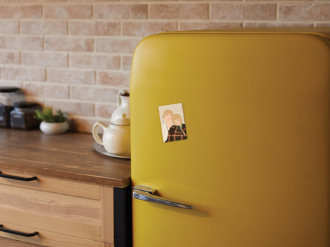 A retro yellow fridge in a cozy kitchen displays the TS Folkevermore Refrigerator Magnet by Onderkast Studio—its small, illustrated charm pops against wood cabinets and a brick backsplash for the perfect touch of folklore.