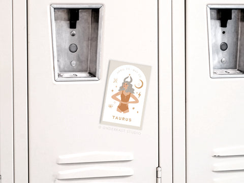 A white locker displays an Onderkast Studio Taurus Zodiac Refrigerator Magnet featuring an illustrated woman with horns, stars, a crescent moon, and the label TAURUS with dates April 20–May 20.