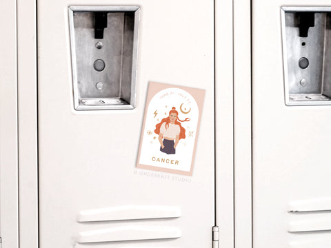 A white locker door displays the Onderkast Studio Cancer Zodiac Refrigerator Magnet, featuring a person holding a crab, “Cancer” label, June 21–July 22 dates, and surrounding astrological symbols.
