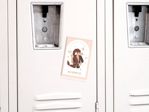 A white locker displays the Onderkast Studio Scorpio Zodiac Refrigerator Magnet, showcasing a stylized scorpion with stars, moons, and dates—capturing Scorpios enigmatic personality.