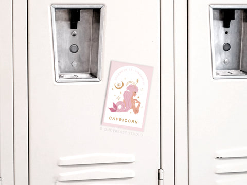 The Onderkast Studio Capricorn Zodiac Refrigerator Magnet features a white locker design with a pastel sticker of a stylized goat, mermaid tail, stars, and crescent moon—a celestial accent for fridges or any metal surface.