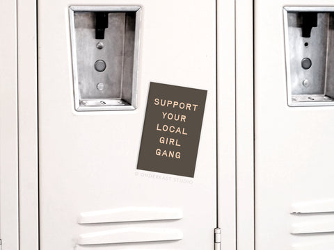 The Support Your Local Girl Gang Magnet by Onderkast Studio features a dark background with white text, celebrating female solidarity and strong women.