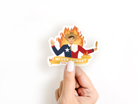 A hand holds the Onderkast Studio Never Forget Blazing Big Tex Sticker, a weatherproof vinyl sticker featuring Big Tex in a Texas-themed suit before flames with a hot dog, perfect for fans of quirky Texas history.