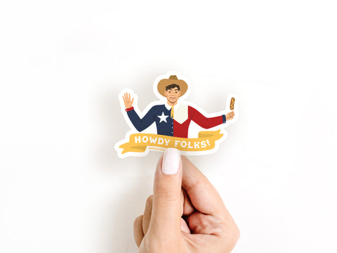 A hand with white nail polish holds the Howdy Folks Sticker by Onderkast Studio, featuring Big Tex in a Texas flag shirt, waving with a Corny Dog and a yellow banner that says Howdy Folks!.