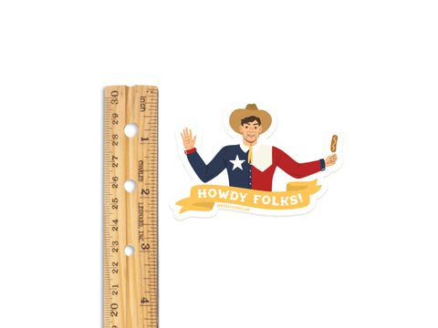 A wooden ruler beside the Onderkast Studio Howdy Folks Sticker shows its 3 size. The die-cut vinyl sticker features a smiling, waving cowboy in a Texas flag shirt holding a Corny Dog with a yellow Howdy Folks! banner.
