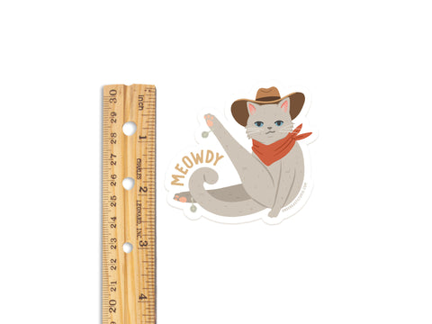 The Meowdy Sticker by Onderkast Studio features a gray cowboy cat in a red bandana and hat with MEOWDY text. This 3-inch die cut vinyl sticker is perfect for fans of cowboy cats!.