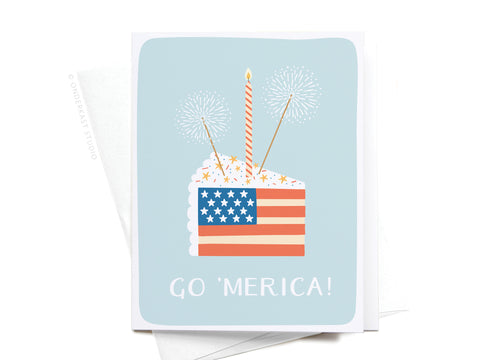 The Go ‘Merica! Greeting Card – FINAL STOCK by Onderkast Studio features a slice of cake decorated as an American flag with a candle and sparklers, plus “GO MERICA!” on a light blue background—perfect for celebrating American pride.