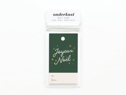 The Joyeux Noël Gift Tag by Onderkast Studio features green and white card stock, gold stars, Joyeux Noël in script, labeled to/from spaces, and comes with twine.