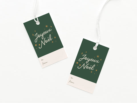 The Onderkast Studio Joyeux Noël Gift Tag features green and cream card stock with gold stars, white string, vibrant Joyeux Noël script, and labeled spaces for to: and from:. Set of two.