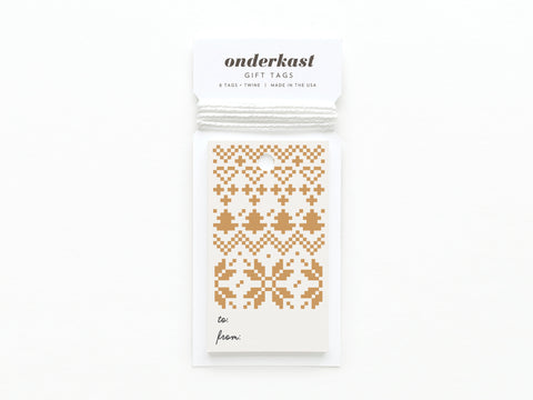 The Holiday Cross Stitch Gift Tag by Onderkast Studio features gold geometric cross-stitch patterns, vibrant colors, and includes white string. Each tag has to: and from: at the bottom and is labeled Onderkast GIFT TAGS.