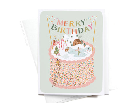 The Merry Birthday Cake Greeting Card by Onderkast Studio features a festive cake topped with a winter ice skating scene and cozy cabins. Colorful sprinkles and banners spelling MERRY BIRTHDAY complete this charming premium card.