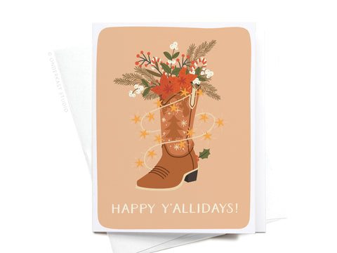 The Happy Y’allidays! Cowboy Boot Greeting Card by Onderkast Studio features a boot filled with festive greenery, flowers, ornaments, and string lights for Southern flair. “Happy Y’allidays!” is printed at the bottom.