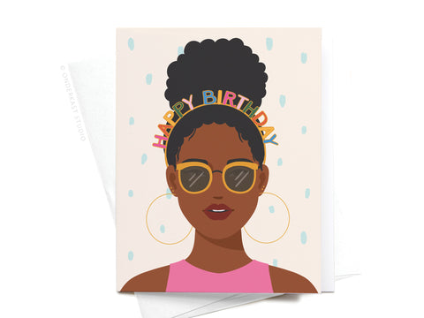 Celebrate in style with Onderkast Studio’s Happy Birthday Headband - Dark, shown on a dark-skinned woman with curly hair in a high bun, hoop earrings, sunglasses, and a pink top amid confetti dots on a light background.