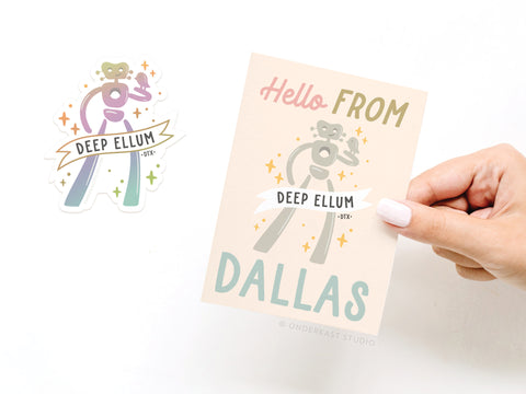 A hand holds Onderkast Studio’s Hello From Dallas Traveling Man Sticker Greeting Card printed on white cardstock, featuring a pastel robot and accompanied by a matching Deep Ellum vinyl sticker on white background.