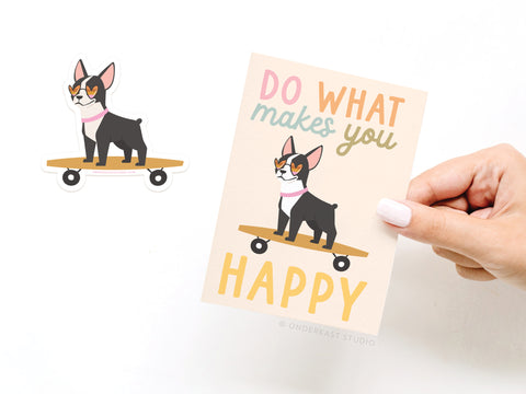 A hand holds Onderkast Studio’s Do What Makes You Happy Dog Sticker Greeting Card, printed on white cardstock with a dog on a skateboard and uplifting message, alongside a matching playful vinyl sticker.