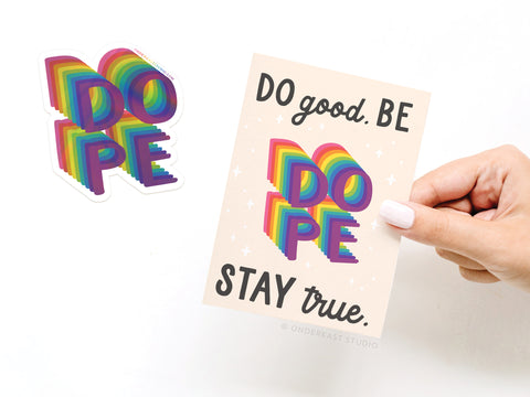 A hand holds the Onderkast Studio Do Good Be Dope Stay True Sticker Greeting Card, featuring “DOPE” in bold 3D rainbow letters. A matching rainbow vinyl sticker is beside the thick white card stock greeting card.