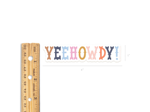 A wooden ruler sits beside the Onderkast Studio Yeehowdy! Sticker, a colorful 4x1 vinyl sticker thats water resistant and durable.